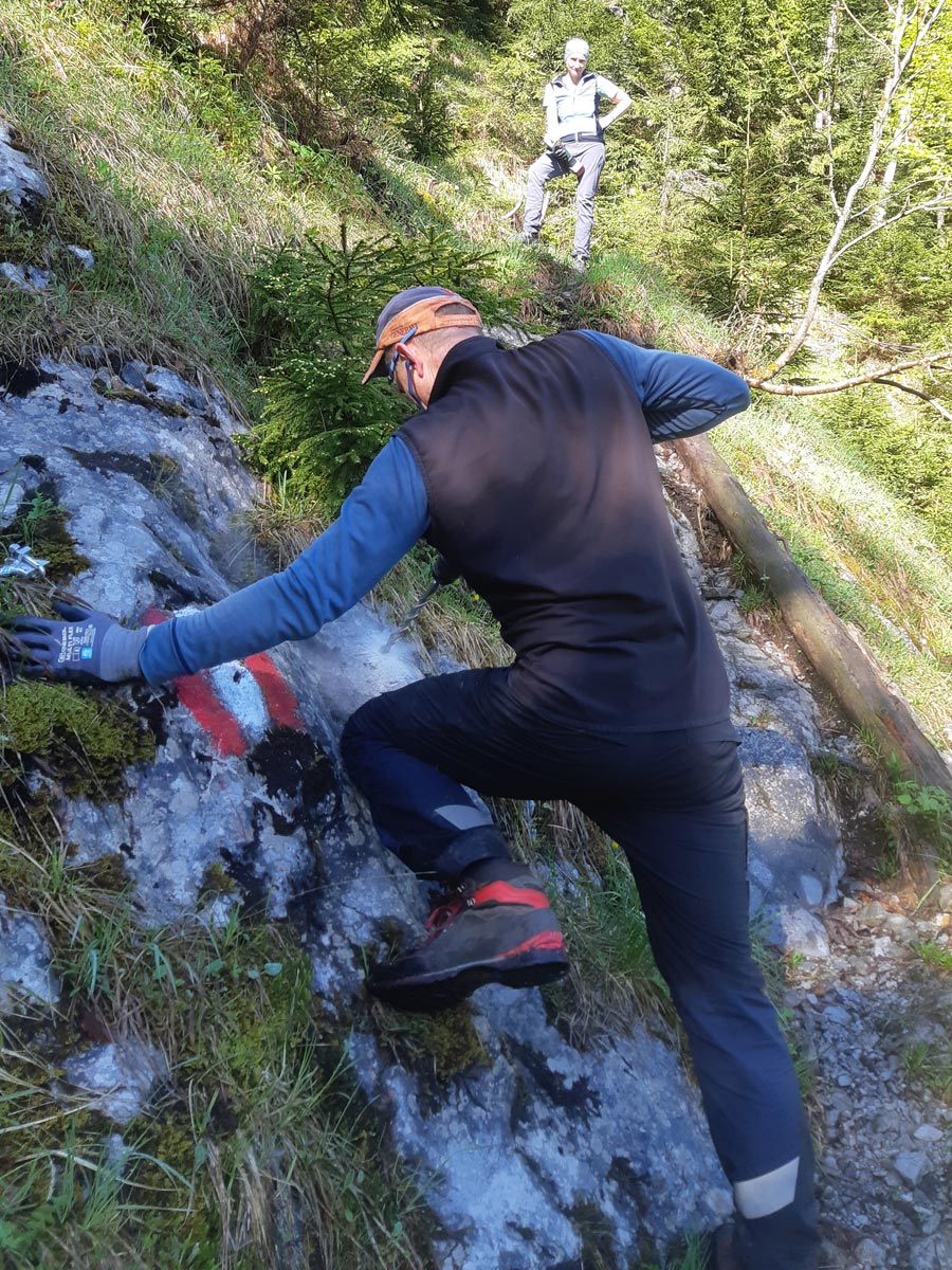 Wegsanierung_Oberscheffau_2 Mann bohrt mit einer Bohrmaschine am Hang in einen Berg um einen Bohrhaken zu befestigen.