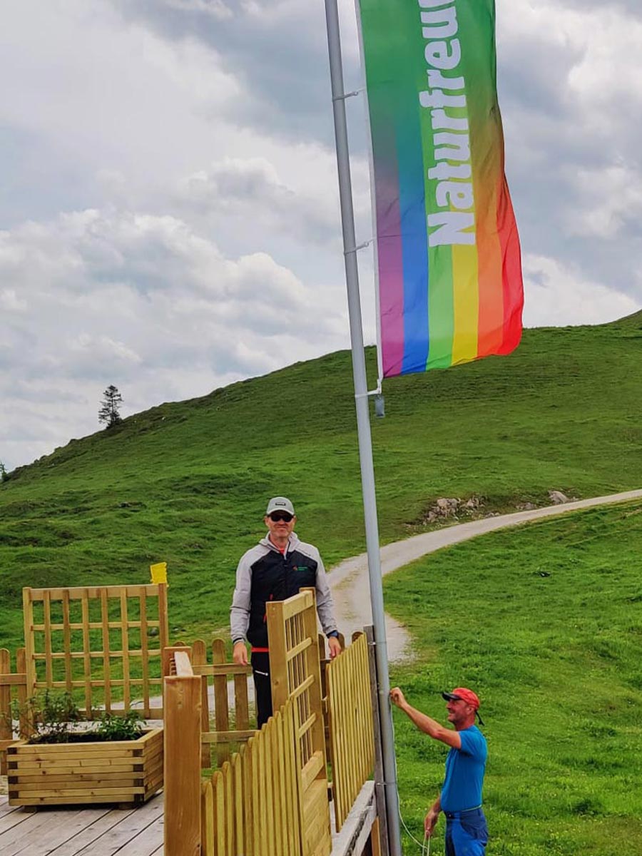 Anton-Proksch-Haus Zwei Männer hängen auf dem Anton Proksch Haus, einer Berghütte, die Naturfreunde Regenbogenflagge auf.