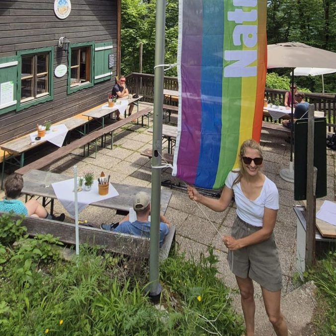 Frau vor Berghütte mit Regenbogenflagge