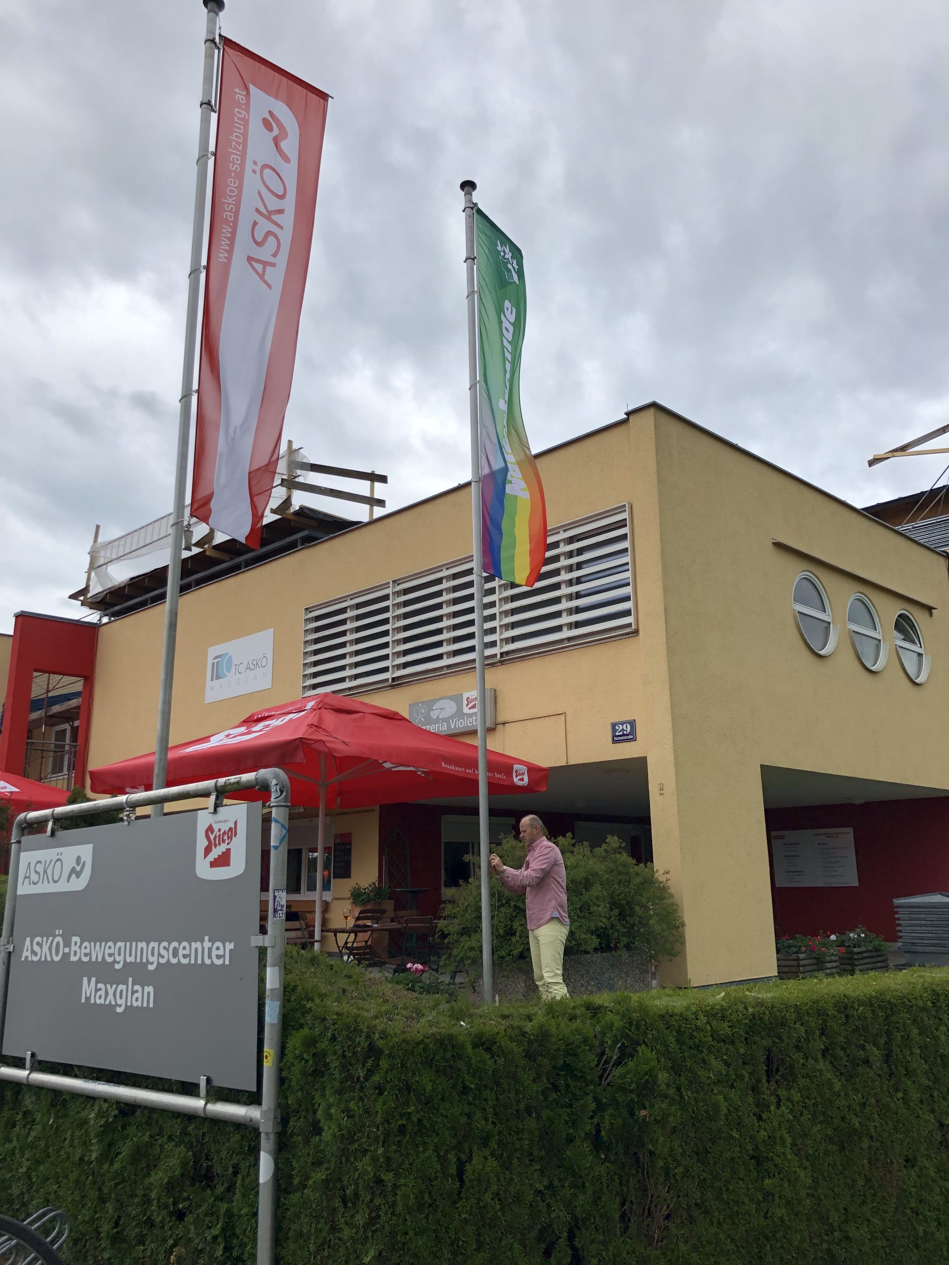 Büro_LO_Maxglan Foto vor dem Büro in Maxglan mit dem Geschäftsführer, der die Pride Flagge schon angebracht hat