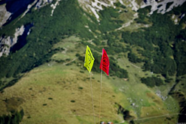 Streckenfahnen Alpin Team Trail 2026 Werfenweng Gelbe und rote Streckenfahne des Alpin Team Trail 2026 auf einer Almwiese in Werfenweng