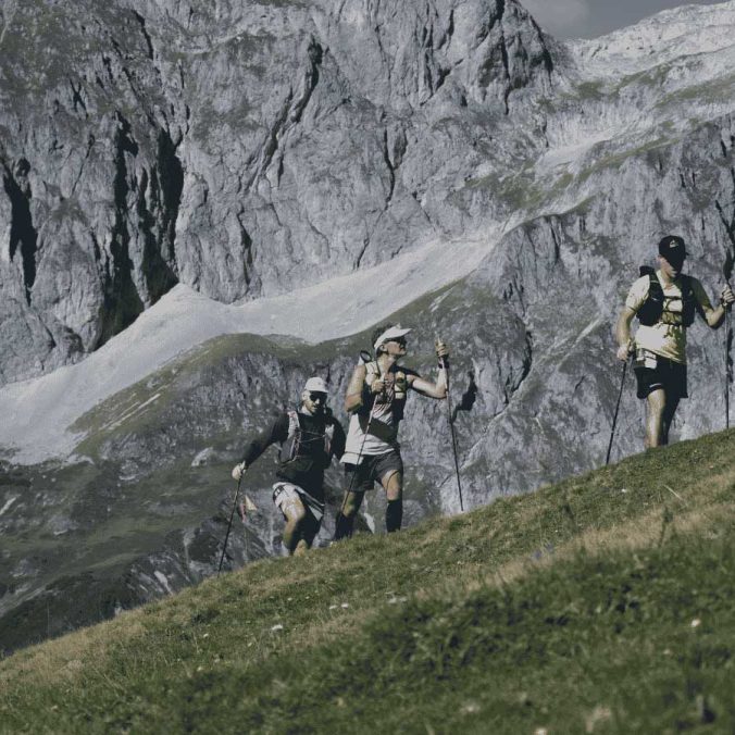 Drei Trailrunner beim Alpin Team Trail 2026 in Werfenweng laufen über eine steile Bergwiese vor einer felsigen Bergkulisse